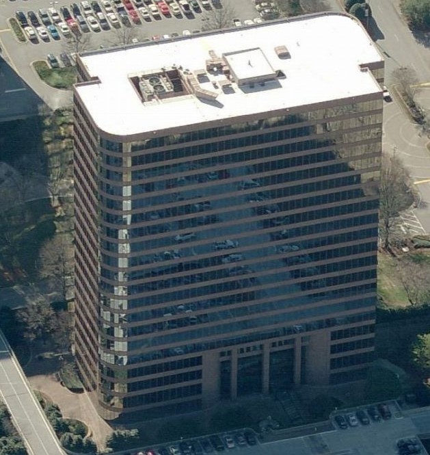Aerial view of a tall, brown glass office building reflecting the surrounding area, with parked cars and trees visible—ideal for showcasing expert commercial roofing or commercial roof repair services.