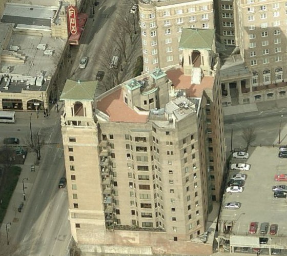 Aerial view of a historic multi-story building with two corner towers, red roofs maintained by a skilled commercial roofer, and arched windows. City streets, parked cars, and the Fox Theater with its red marquee sign are nearby.
