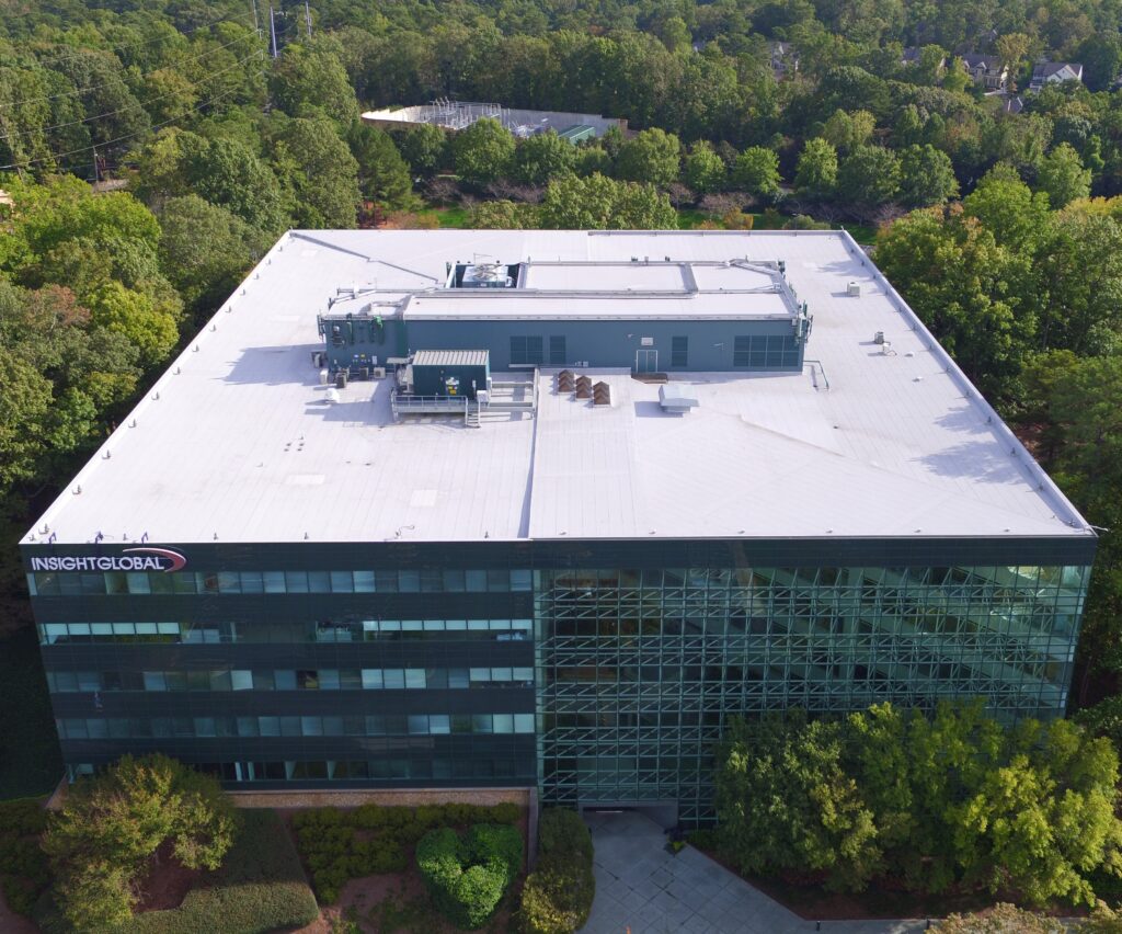 Aerial view of a modern office building surrounded by trees, featuring a white commercial roofing system and large glass windows. The Insight Global sign is visible on one corner of the building.