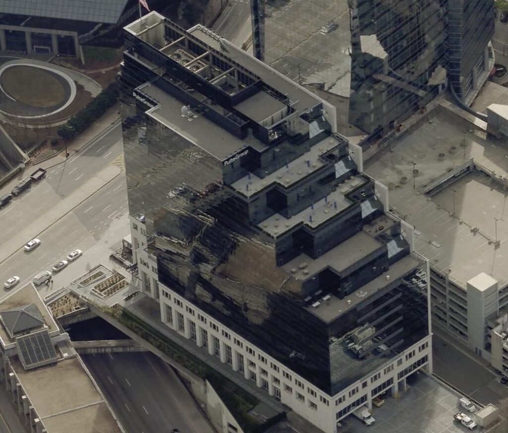 Aerial view of a modern, black glass office building with staggered layers and rooftop structures highlights the expertise of a roofing contractor, surrounded by roads, cars, and nearby urban buildings.
