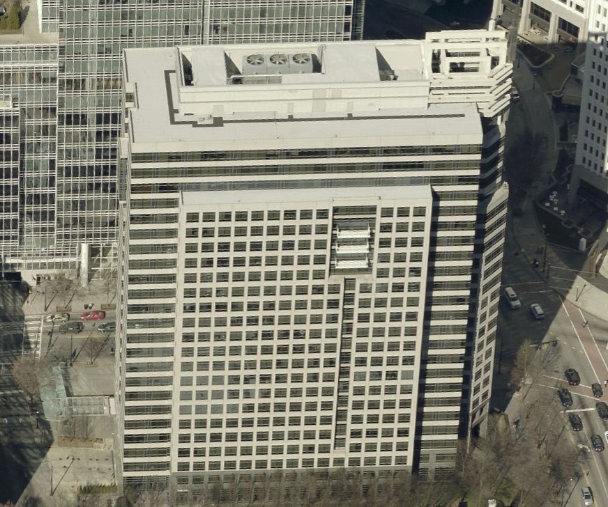 Aerial view of a modern, rectangular office building with large windows and a rooftop maintained by a commercial roofer, filled with HVAC units, surrounded by city streets and other office buildings.