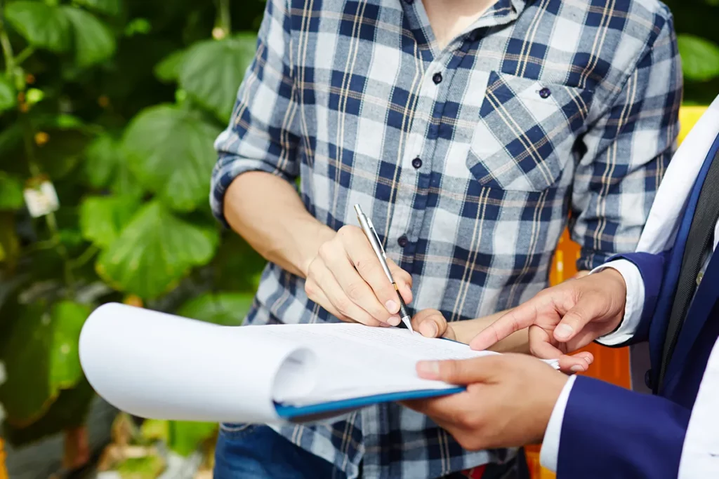 Two people reviewing a document on a clipboard in a greenhouse.