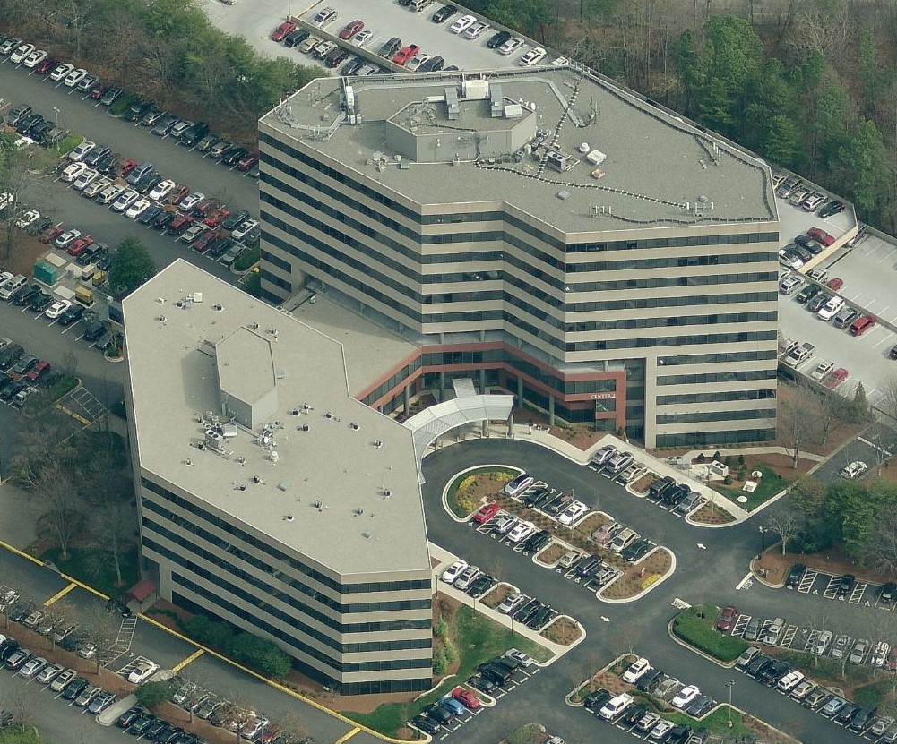 Aerial view of two connected, multi-story office buildings surrounded by several parking lots filled with cars.