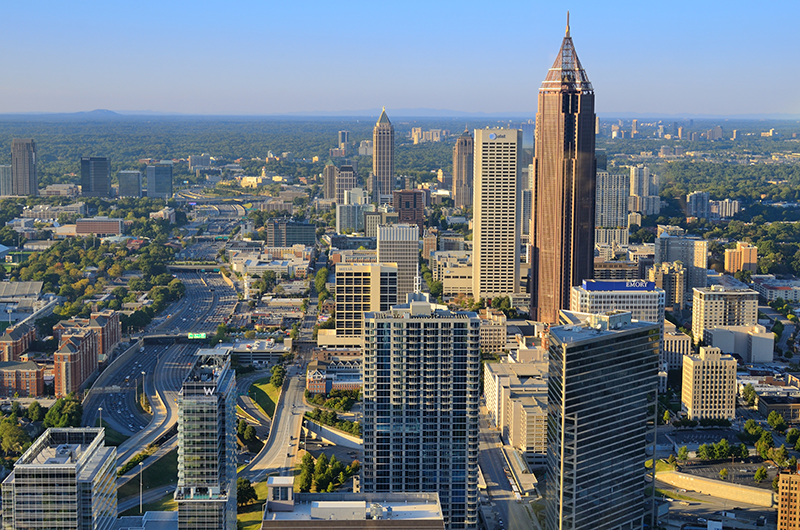 Aerial view of the Atlanta skyline at sunset, featuring the Bank of America Plaza skyscraper surrounded by other buildings and city highways.