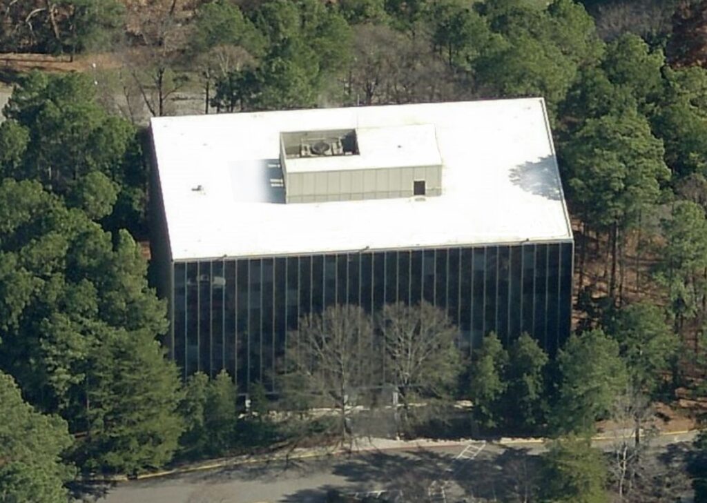 Aerial view of a rectangular office building with a flat roof, surrounded by a dense forest.