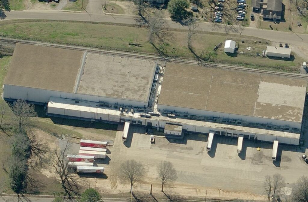Aerial view of a large rectangular warehouse with several loading docks and semi-trailers parked in the lot.