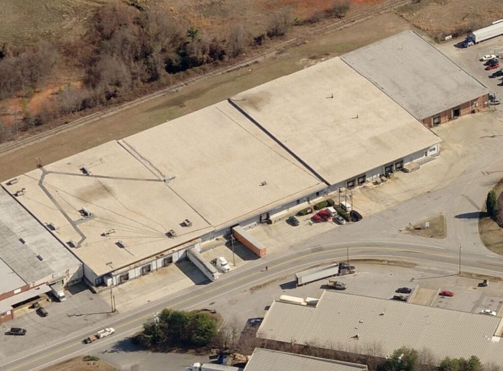 Aerial view of a long industrial warehouse with loading docks, semi-trucks, and a surrounding parking area.