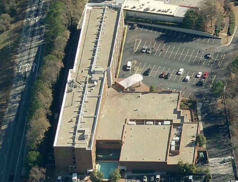 Aerial view of a long, multi-story brick building with a parking lot and a nearby road.