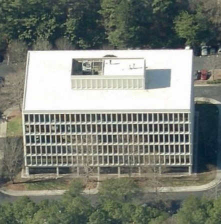 Aerial view of a rectangular office building with a grid-patterned exterior and a flat white roof.