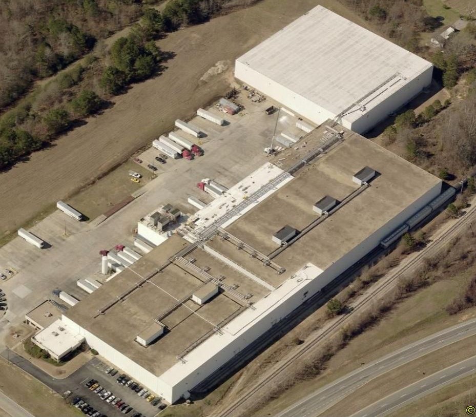 Aerial view of a large industrial warehouse complex with semi-trucks parked in the loading bays and a nearby highway.