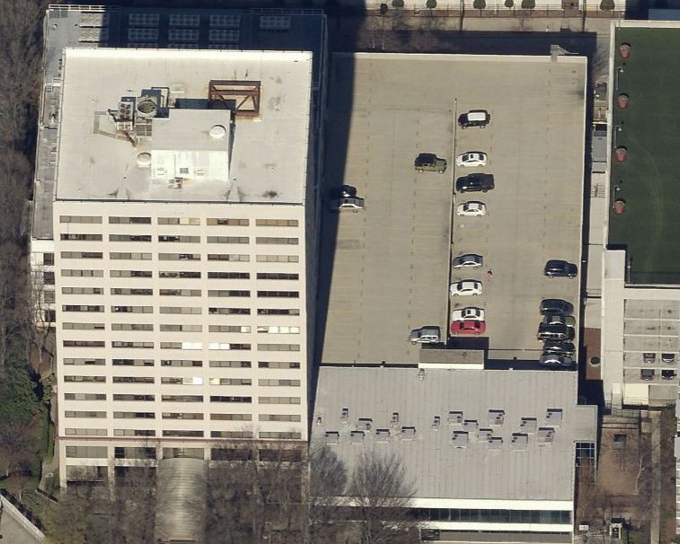 Aerial view of a rectangular office building next to a surface parking lot with several parked cars.