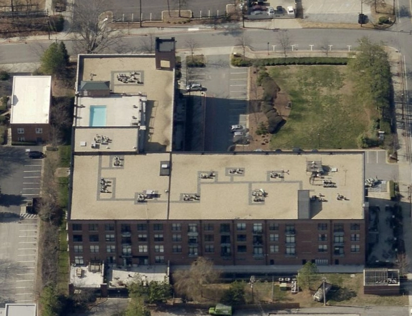 Aerial view of a multi-story brick apartment building featuring a rooftop pool and surrounding parking lots.