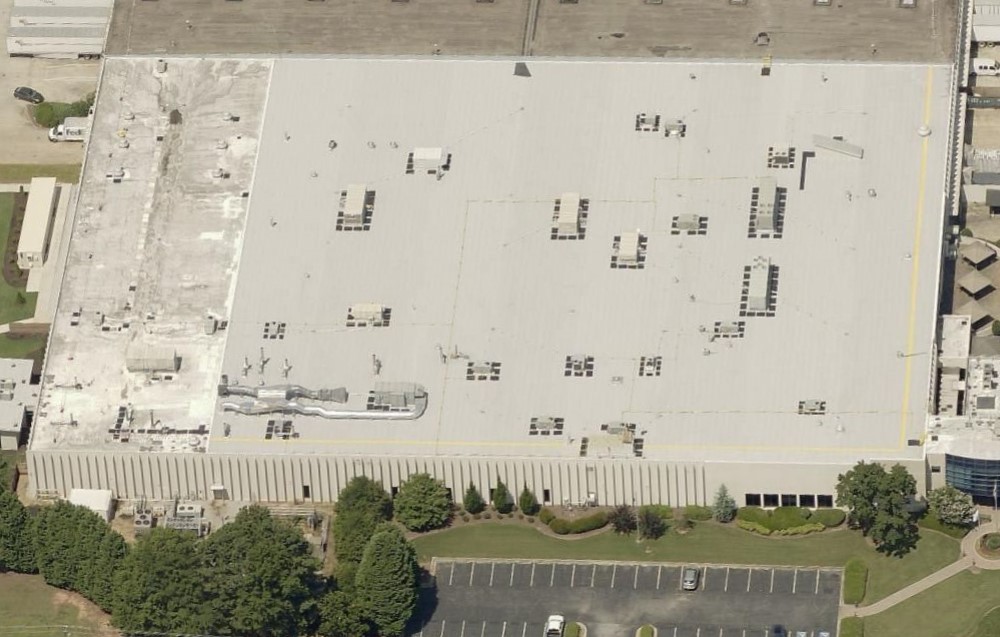 Aerial view of a large rectangular warehouse with a light-colored flat roof featuring multiple HVAC units.