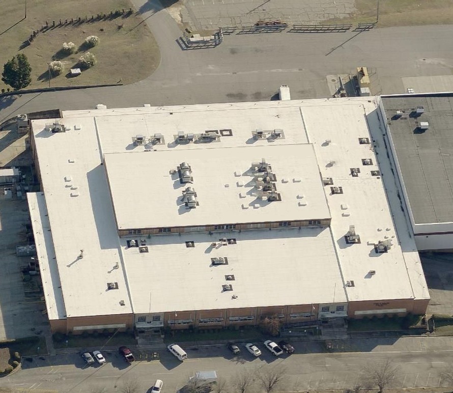 Aerial view of a large, flat-roofed commercial building with multiple rooftop HVAC units and a parking lot in front.