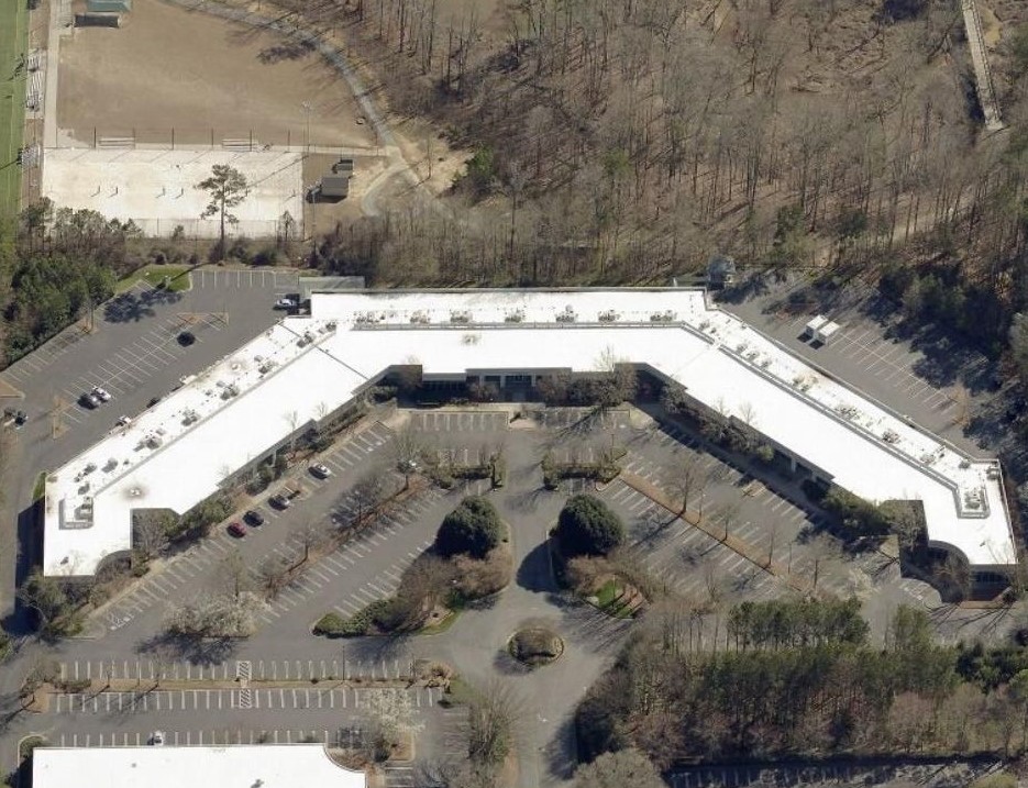Aerial view of a V-shaped commercial building surrounded by a parking lot and wooded area.