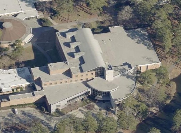 Aerial view of a large complex of connected buildings surrounded by a wooded area.