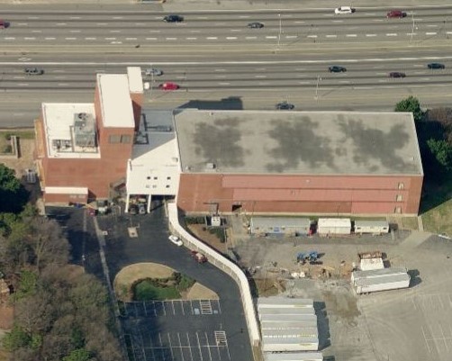 Aerial view of a brick industrial building adjacent to a multi-lane highway.