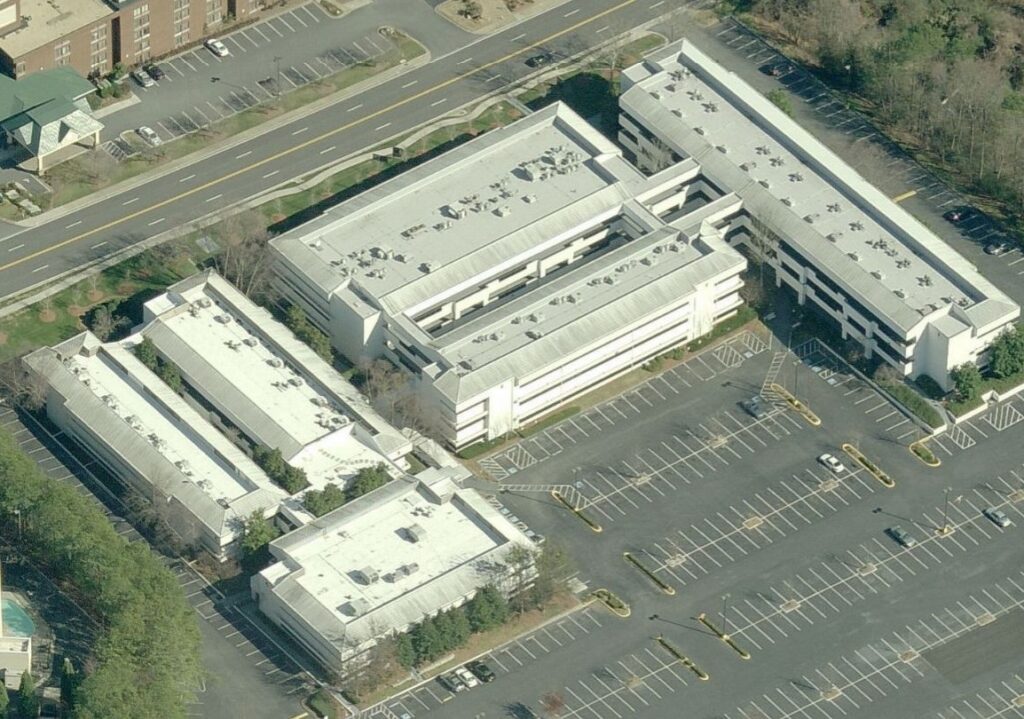 Aerial view of a multi-building office complex with white roofs and an adjacent parking lot.