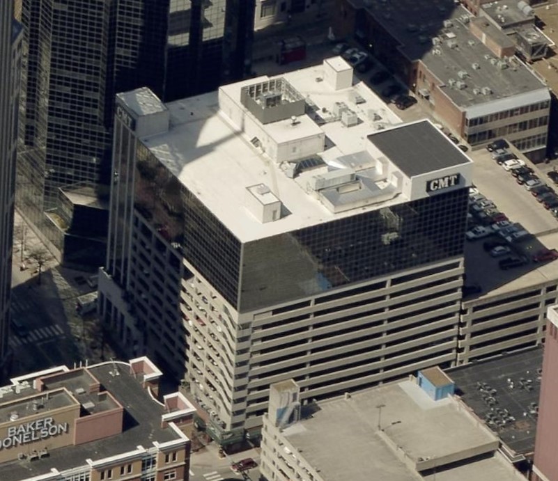 Aerial view of an office building with the CMT logo on the roof, featuring a parking garage base and neighboring city structures.
