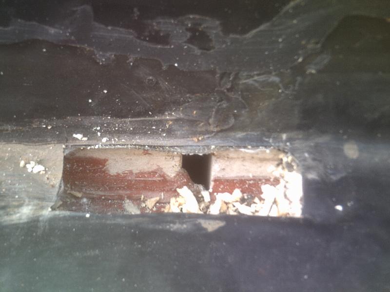 A rectangular gap in a dark surface reveals a view of interior brickwork with debris at the base.