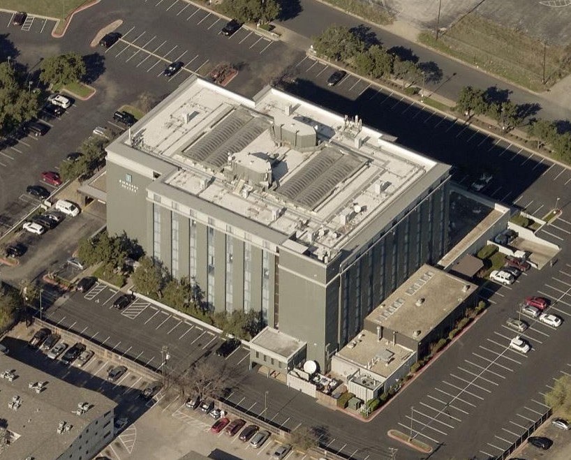 Aerial view of a multi-story hotel building surrounded by large parking lots filled with cars.