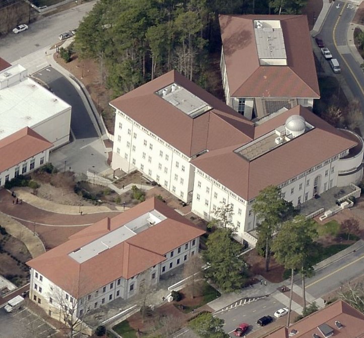 Aerial view of a university campus featuring white buildings with red roofs, surrounded by trees, sidewalks, and roads.