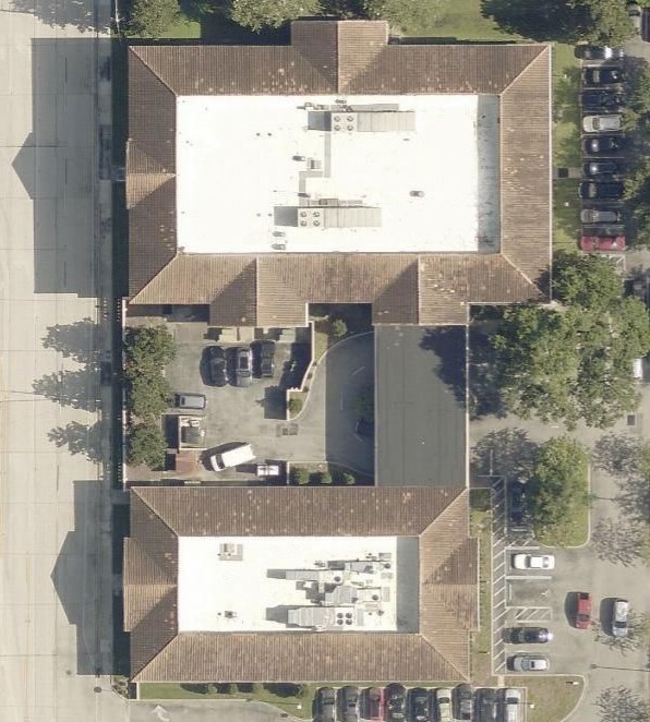 Aerial view of two rectangular commercial buildings with tile roofs and parking lots on three sides.