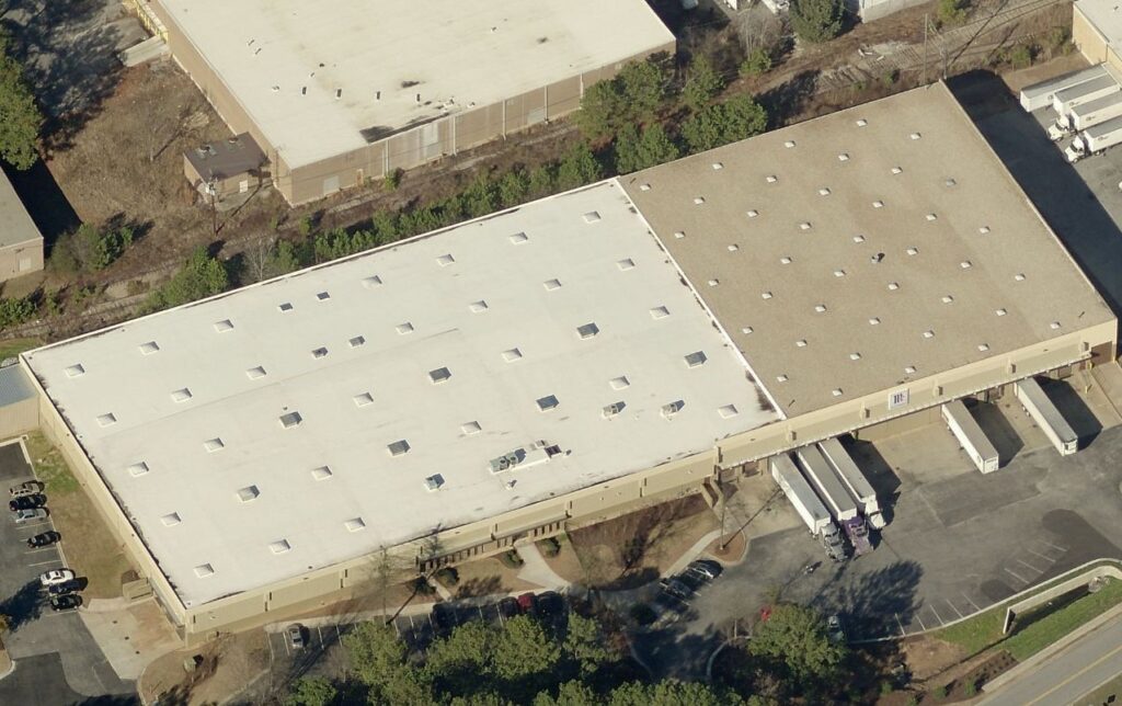 Aerial view of a large warehouse with a flat roof, loading docks, and several semi-trailers parked in the lot.