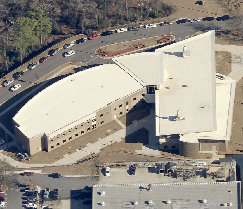 Aerial view of a commercial building with a curved wing and a flat-roofed section, surrounded by parking lots.