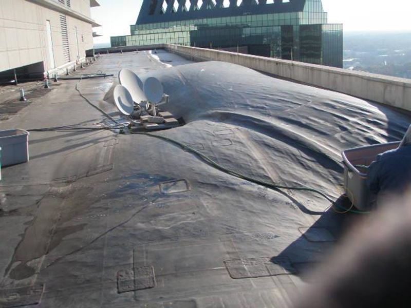 A large, dark, membrane-covered mound on a building rooftop with several satellite dishes.