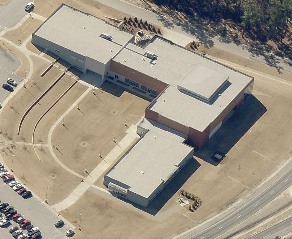 Aerial view of a large L-shaped building with a parking lot and curved walkways.