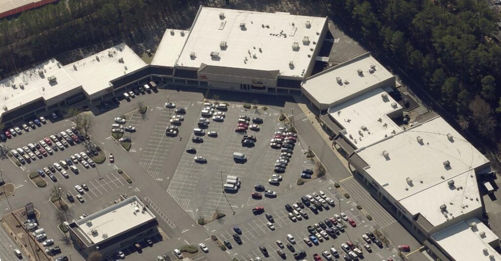 Aerial view of a U-shaped shopping center building complex with a large central parking lot filled with cars.