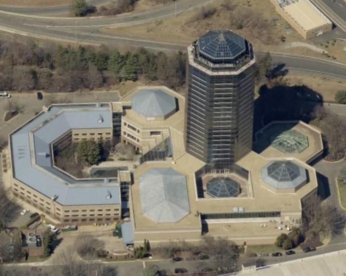 Aerial view of a tall, octagonal office tower connected to several lower buildings with various roof shapes and skylights.