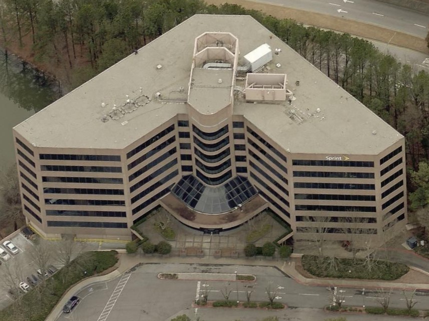 Aerial view of a V-shaped office building with the Sprint logo on the side, surrounded by trees and a parking lot.