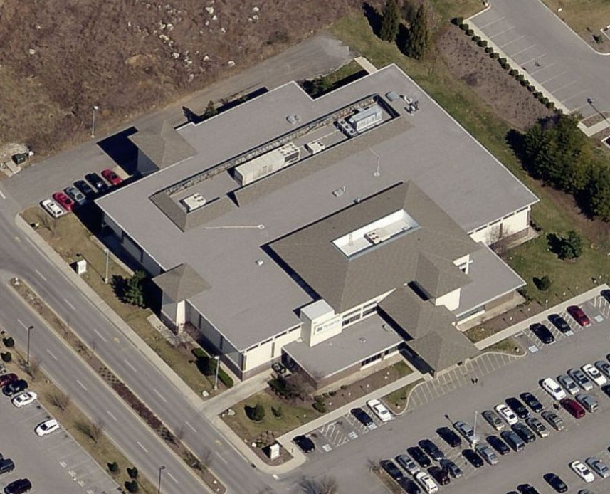 Aerial view of a multi-winged commercial building with a grey roof, surrounded by parking lots and access roads.