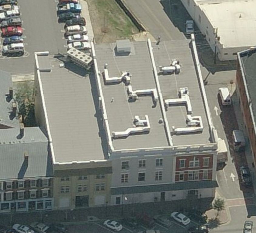 Aerial view of a city block featuring a flat-roofed building with multiple HVAC units and nearby street parking.