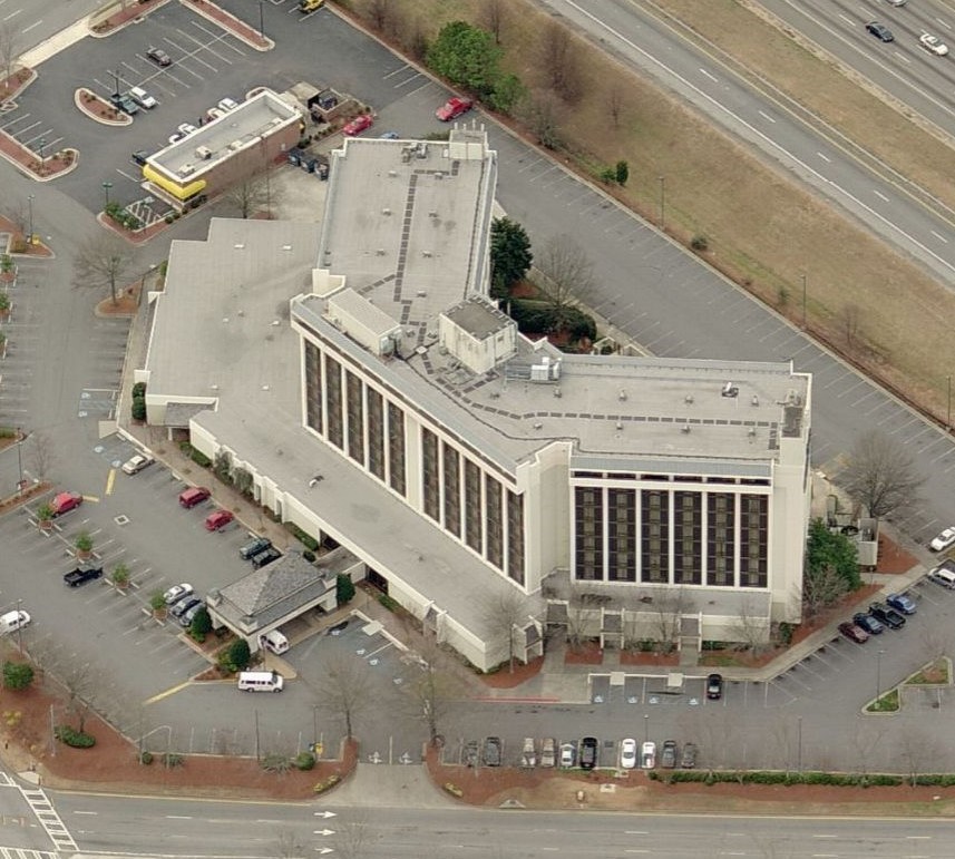 Aerial view of a multi-story hotel with a U-shaped roof and surrounding parking lots.